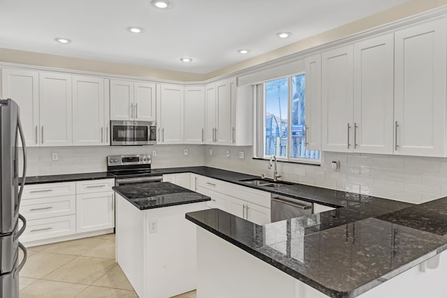 kitchen with appliances with stainless steel finishes, sink, white cabinets, dark stone countertops, and a kitchen island