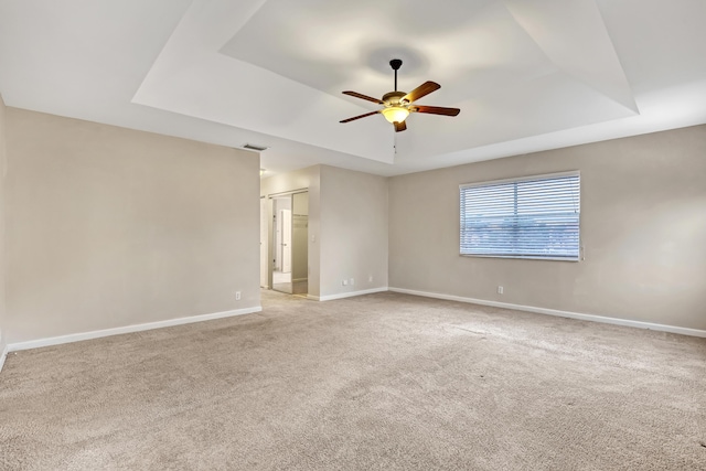 unfurnished room featuring ceiling fan, light carpet, and a tray ceiling