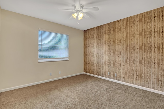 carpeted empty room with ceiling fan and wood walls