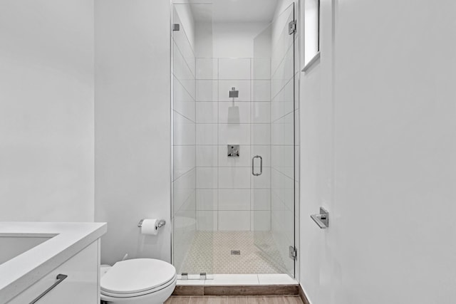 bathroom with hardwood / wood-style floors, a shower with door, toilet, and vanity