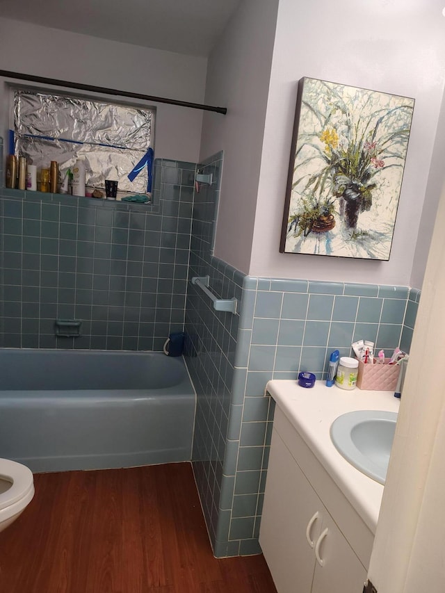 full bathroom with toilet, hardwood / wood-style floors, tile walls, vanity, and tiled shower / bath