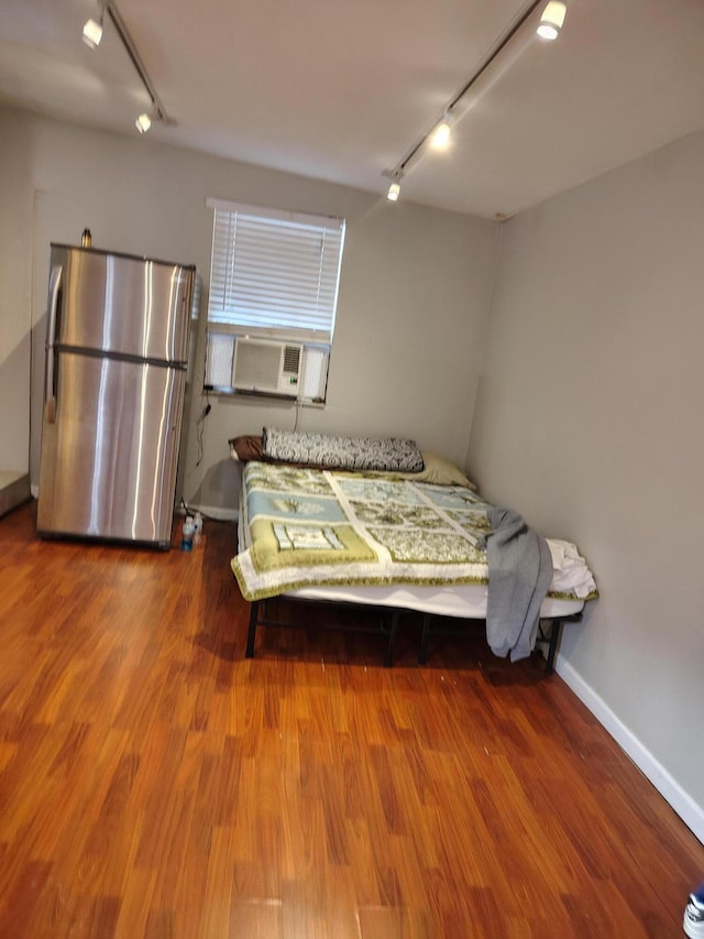 bedroom with cooling unit, rail lighting, hardwood / wood-style flooring, and stainless steel fridge