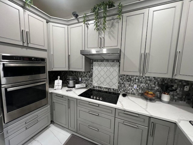 kitchen featuring double oven, light stone countertops, gray cabinets, black electric cooktop, and decorative backsplash