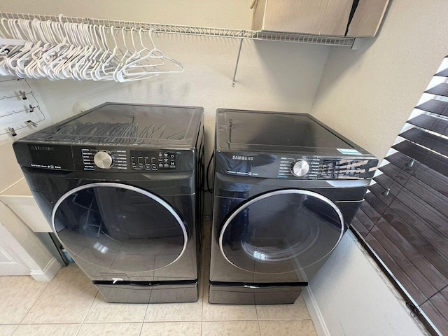 clothes washing area with cabinets, tile patterned floors, and washer and clothes dryer