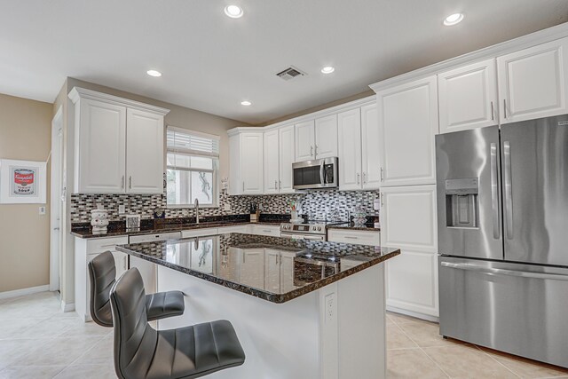 kitchen featuring visible vents, white cabinets, appliances with stainless steel finishes, a center island, and dark stone counters