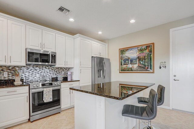 kitchen with visible vents, white cabinets, a kitchen island, dark stone countertops, and stainless steel appliances