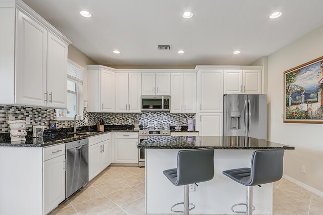 kitchen with a center island, stainless steel appliances, visible vents, white cabinets, and dark stone counters