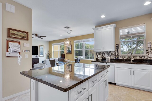 kitchen with white dishwasher, a sink, visible vents, a kitchen island, and white cabinetry