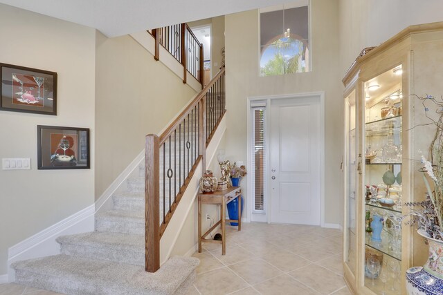 foyer featuring a towering ceiling, light tile patterned floors, stairs, and baseboards