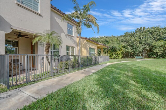 view of side of home with a lawn, fence, a ceiling fan, and stucco siding