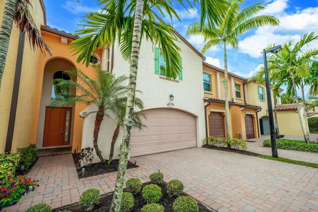 mediterranean / spanish-style home featuring an attached garage, a tile roof, decorative driveway, and stucco siding