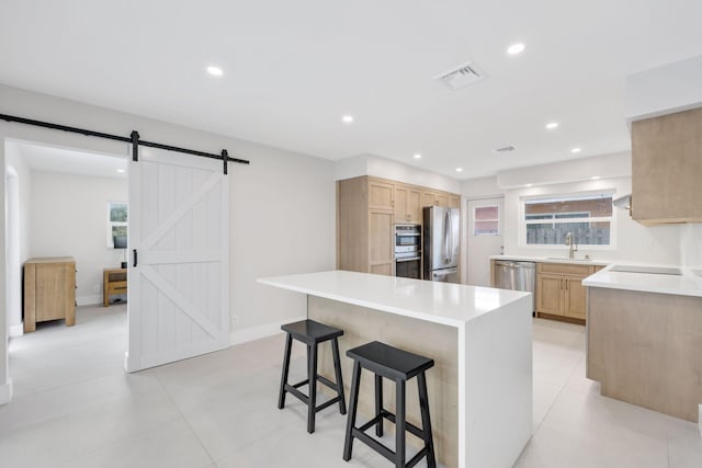 kitchen featuring light brown cabinets, a breakfast bar, a barn door, and appliances with stainless steel finishes