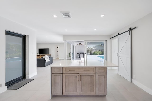 kitchen featuring light tile patterned floors, ceiling fan, a center island with sink, a barn door, and light brown cabinets