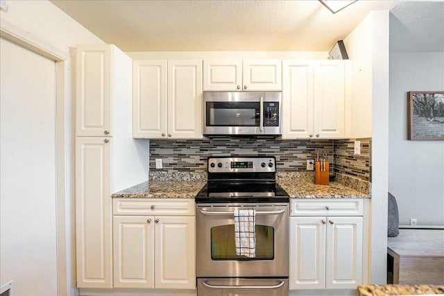 kitchen with stainless steel appliances, stone countertops, white cabinets, and backsplash