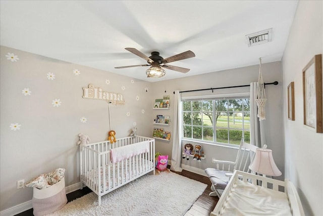 bedroom with a crib, hardwood / wood-style flooring, and ceiling fan