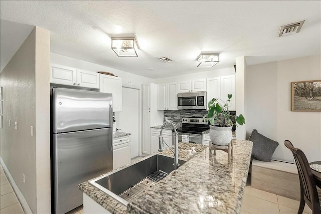 kitchen featuring light tile patterned flooring, sink, stainless steel appliances, decorative backsplash, and white cabinets