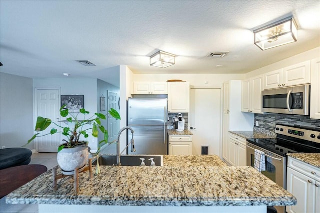 kitchen with sink, white cabinetry, stainless steel appliances, light stone countertops, and decorative backsplash