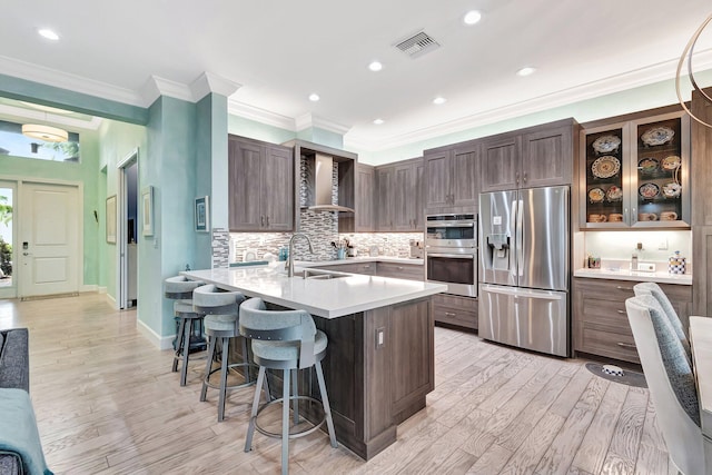 kitchen with wall chimney exhaust hood, dark brown cabinetry, sink, appliances with stainless steel finishes, and a kitchen breakfast bar