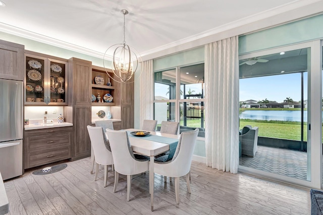 dining room featuring crown molding, a water view, an inviting chandelier, and light wood-type flooring