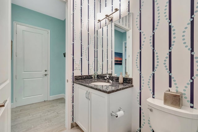 bathroom with toilet, vanity, and wood finished floors