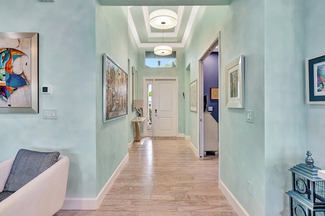 hallway with crown molding, light wood-style flooring, a high ceiling, and baseboards