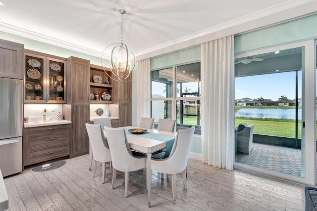 dining area featuring a water view, ornamental molding, light wood-style flooring, and an inviting chandelier