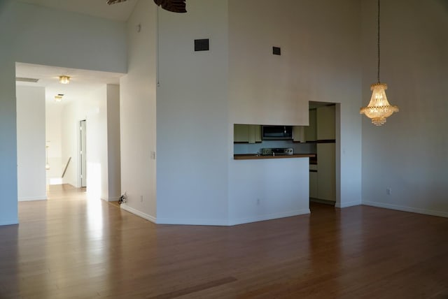 unfurnished living room featuring a high ceiling, wood-type flooring, and an inviting chandelier