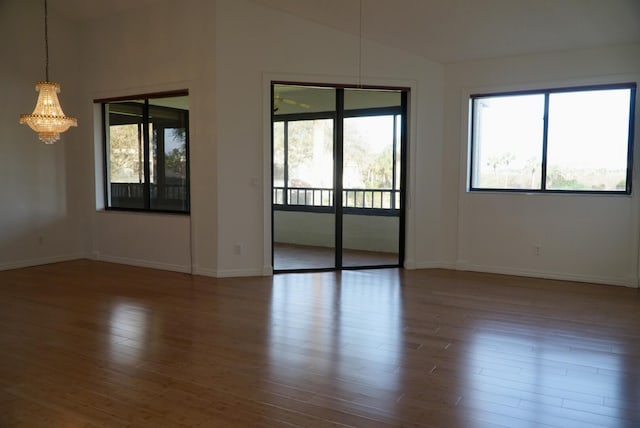 empty room with hardwood / wood-style floors, lofted ceiling, and an inviting chandelier