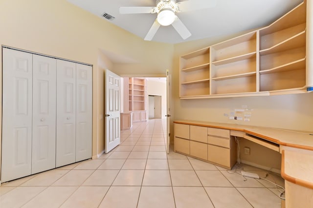 unfurnished office featuring light tile patterned floors, built in desk, and ceiling fan