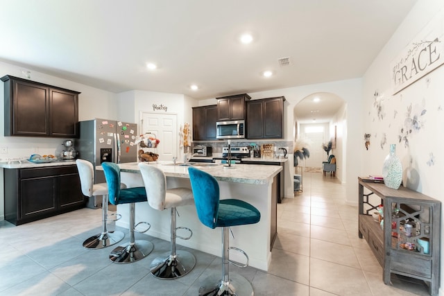 kitchen featuring a breakfast bar area, an island with sink, dark brown cabinetry, and appliances with stainless steel finishes