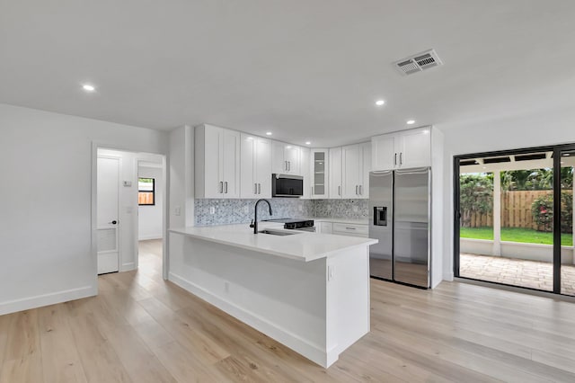 kitchen featuring white cabinetry, backsplash, light hardwood / wood-style floors, kitchen peninsula, and stainless steel refrigerator with ice dispenser