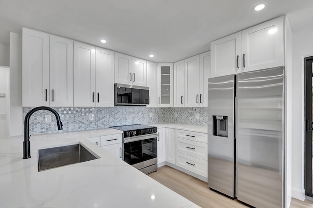 kitchen featuring white cabinetry, sink, stainless steel appliances, light stone countertops, and light wood-type flooring