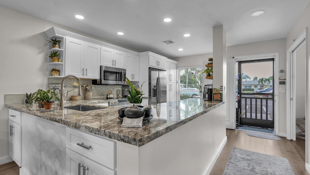 kitchen featuring kitchen peninsula, appliances with stainless steel finishes, sink, white cabinetry, and light stone counters