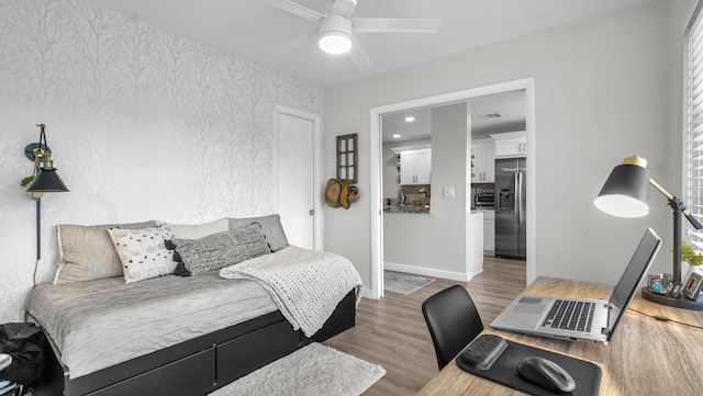 bedroom with ceiling fan, hardwood / wood-style flooring, and stainless steel fridge