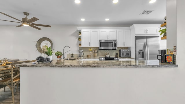 kitchen featuring white cabinets, stainless steel appliances, dark stone countertops, and kitchen peninsula