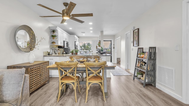 kitchen with light wood-type flooring, white cabinetry, ceiling fan, and light stone counters