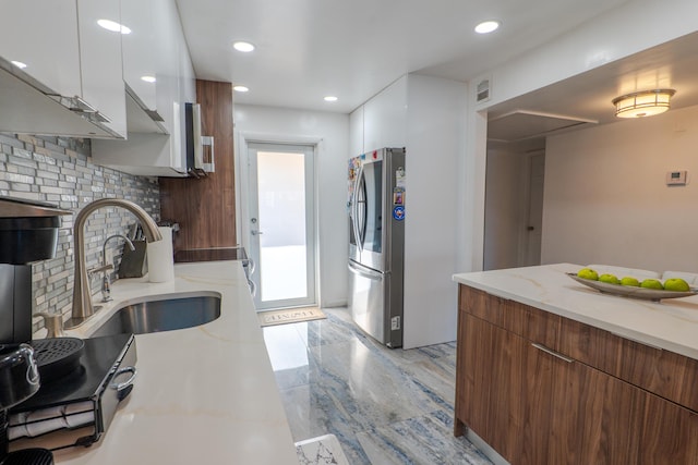 kitchen with sink, stainless steel refrigerator, white cabinetry, light stone counters, and decorative backsplash