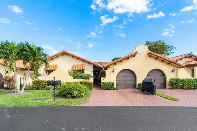 mediterranean / spanish house with a garage, a tile roof, decorative driveway, stucco siding, and a front lawn