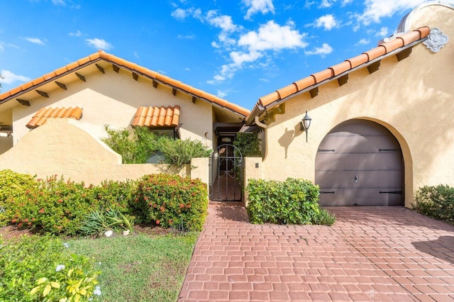 mediterranean / spanish-style house featuring a gate, decorative driveway, a tile roof, and stucco siding