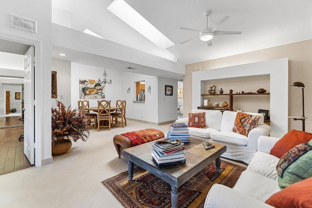 living room with built in shelves, lofted ceiling with skylight, ceiling fan, and a textured ceiling