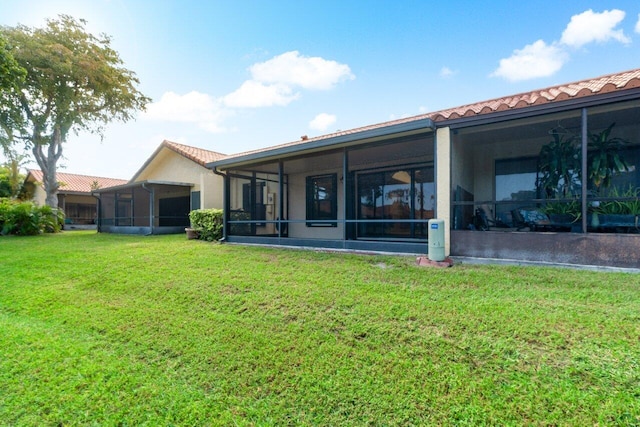 back of house featuring a lawn, a tile roof, and a sunroom