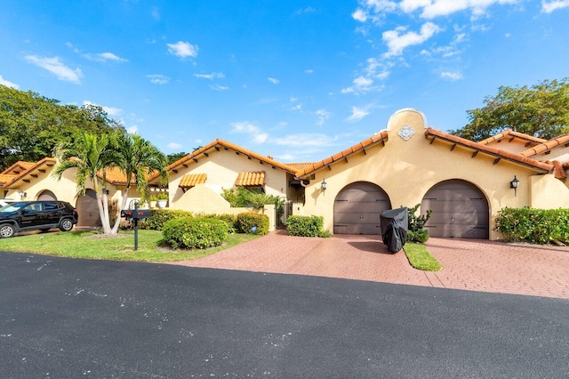 mediterranean / spanish home featuring an attached garage, a tiled roof, decorative driveway, and stucco siding