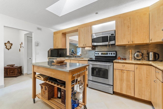 kitchen with appliances with stainless steel finishes, a skylight, tasteful backsplash, sink, and light brown cabinets