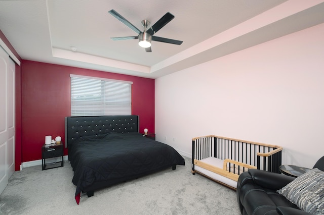 carpeted bedroom with a tray ceiling, a closet, and ceiling fan