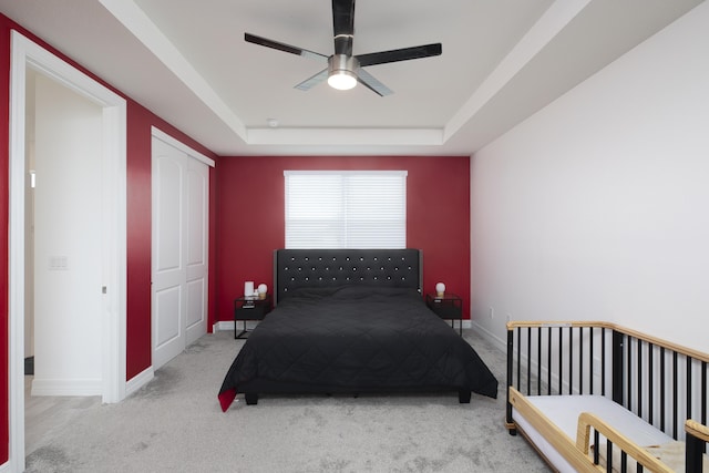 bedroom featuring ceiling fan, light colored carpet, and a tray ceiling