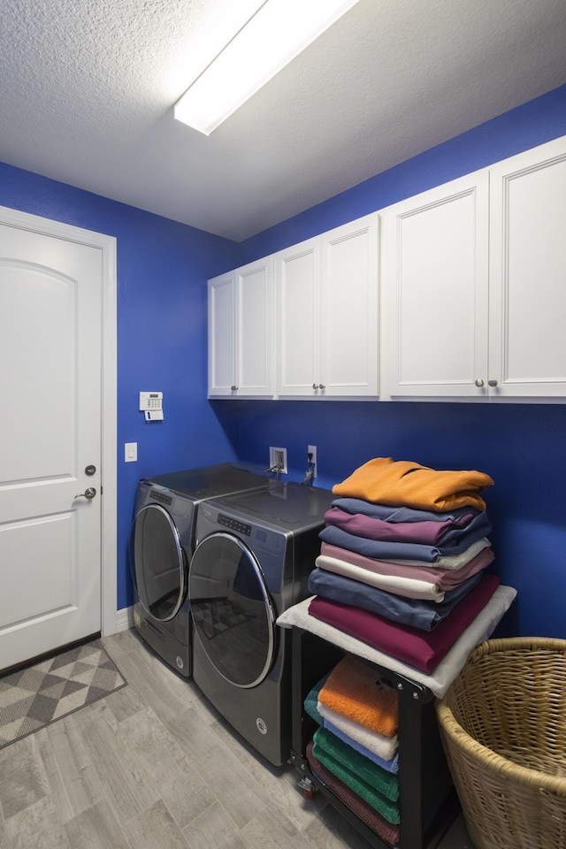 clothes washing area featuring cabinets, independent washer and dryer, a textured ceiling, and light wood-type flooring