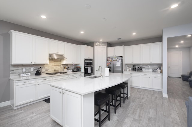 kitchen with appliances with stainless steel finishes, sink, white cabinets, a kitchen breakfast bar, and a center island with sink