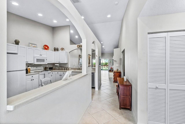 kitchen featuring white cabinetry, a high ceiling, light tile patterned floors, kitchen peninsula, and white appliances