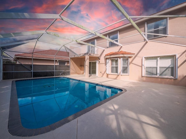 pool at dusk featuring a patio and glass enclosure