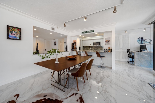 dining area with ornamental molding, rail lighting, and sink